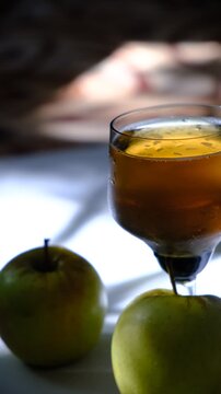 Glass of brut apple cider from Normandy. White table with casting shadows and sunlight. Ripe yellow fruits on the table. Atmospheric mood.	
