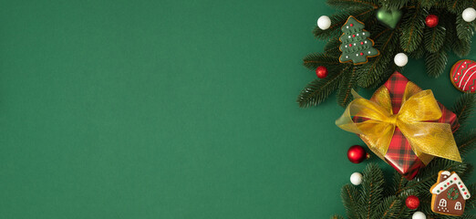 Christmas composition, lush green spruce branches, gift box with a golden bow, gingerbread cookies, red Christmas tree balls and white snowballs. Holiday frame, space for text, flat lay, top view, New