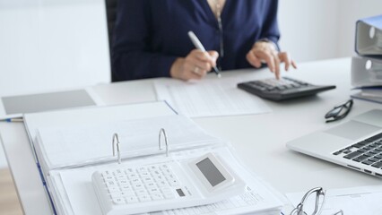 Close up of white calculator over financial documents opposite businesswoman calculating taxes at...