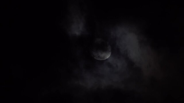 A bright moon partially obscured by clouds illuminates the dark sky, creating a gloomy atmosphere.
