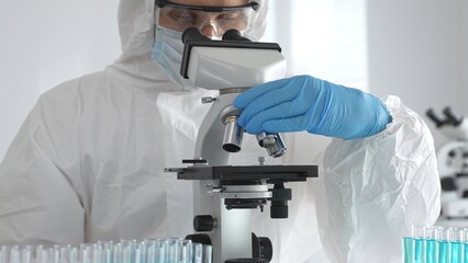 Medical virologist in protective hazmat gear examining viral samples under a microscope while conducting research in a sterile laboratory environment