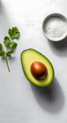 Fresh avocado half with seed, cilantro leaf, and salt in a bowl on a white surface, showcasing healthy food ingredients and natural produce
