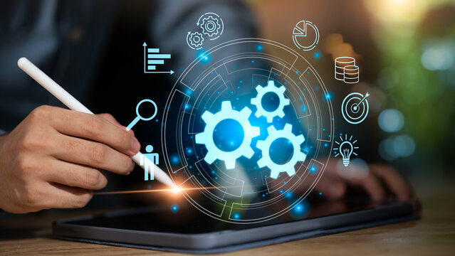 A businessman using a digital tablet with glowing gear icons, representing workflow automation, business process management, innovation, and efficiency powered by modern digital technology. - Powered by Adobe