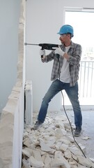 Man construction worker wearing grey checked shirt and blue hardhat is demolishing a wall with a...