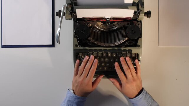 Man's hands adjusting white paper and preparing to type on an old retro typewriter, viewed from above, representing classic communication and storytelling