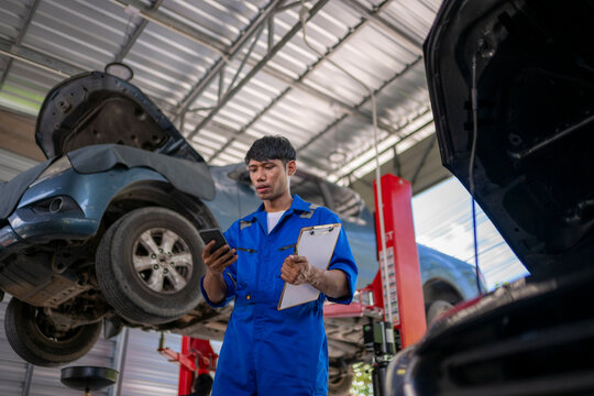 Mechanic using smartphone checking car repair information in garage - Powered by Adobe