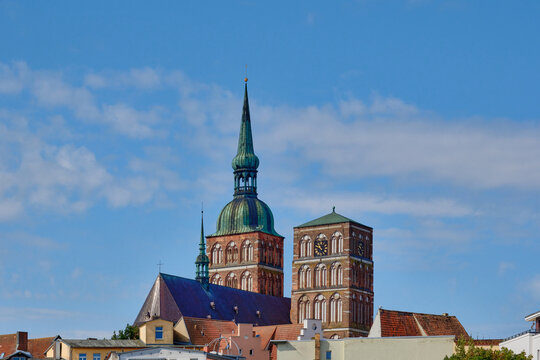 Historic Nikolaikirche in Stralsund, Germany, with its distinctive brick Gothic architecture and spires rising above old town rooftops against a blue sky. Beautiful landmark of Hanseatic heritage