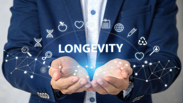 Businessman hands cupping glowing holographic longevity text surrounded by futuristic icons including DNA apple heart calendar globe pencil recycling lightbulb network in neutral studio evoking 