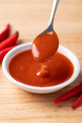 Sriracha sauce in a bowl with spoon on wooden background, Chili sauce