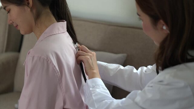 A woman is getting her hair done by a doctor. The doctor is wearing a white coat and is holding a pair of scissors. The woman is sitting on a couch