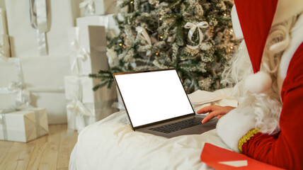 Santa Claus using a laptop to check his list near a Christmas tree