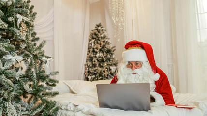 Fototapeta premium santa claus using a laptop computer in a festive christmas setting