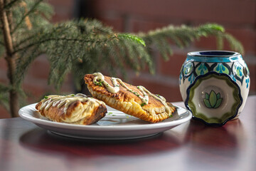 Frontal photograph of empanadas with sauce seen from the front on a white plate on a Corinthian table