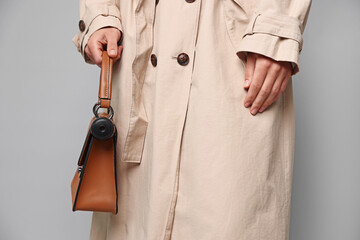Young woman with hidden spy camera in bag on light grey background, closeup