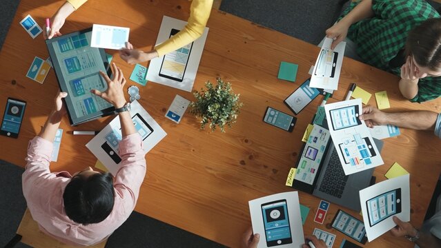Team working at Ux Ui design for mobile phone interface while manager hand out document about wireframe prototype. Top view of project manager explain or brainstorm idea about software. Convocation.