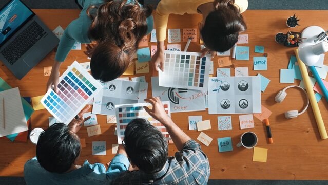 Top view of smart manager writing at logo and sharing idea while designer holding and looking at palette and choose color for logo or product. Aerial view of business team working together. Symposium.