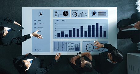 A group of business professionals collaboratively analyzing comprehensive data charts during a strategy meeting in a contemporary office setting. Axiom