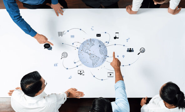 A diverse business team collaborates over a table with visual elements representing global communication and technology, highlighting teamwork and innovation. Trope