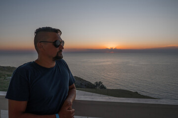 A man in sunglasses swims in a blue pool. Vacation at the hotel by the sea, sunset and mountains. Happy dad, family happiness. Muscles and a beautiful figure, black hair. High quality photo