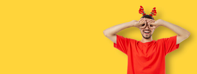 Young man playfully poses with hands around eyes wearing antlers