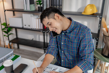 A young architect is multitasking at his desk, sketching blueprints, making phone calls, and reviewing notes. His workspace shows focus, productivity, and modern design work.