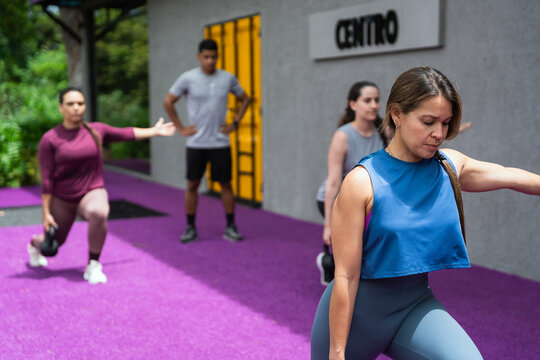Group of latin american people doing lunges with kettlebells during an outdoor fitness class, focusing on strength and wellness