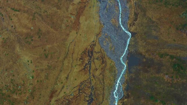 An aerial shot of a river meandering through a vast, brown landscape. The river's path is carved through a barren, mountainous terrain, showcasing the raw, natural beauty of the region.