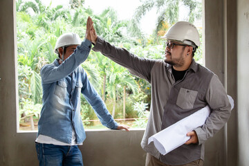 Portrait of two engineers or architects male, with safety helmets and laptop, collaborating on-site, reviewing digital blueprints and discussing the next steps in the construction project, men at work