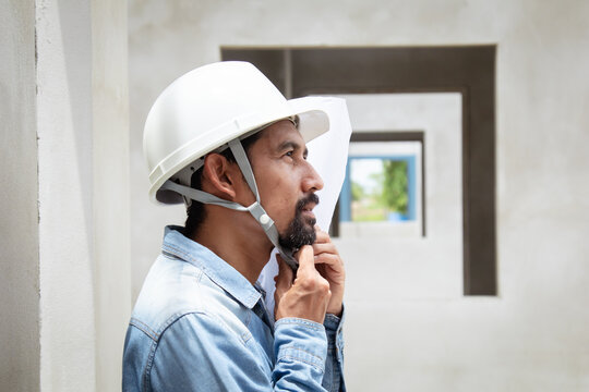 Indian or Asian middle-aged architect man with mustache wearing safety helmet hard hat close up medium shot, professional engineer foreman worker male hold blueprints standing at construction site