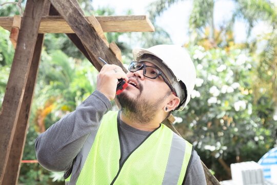 Portrait young Asian engineering architect foreman male wearing safety vest and helmet using walkie-talkie radio on construction site, contractor modern working holding tablet technology, men at work - Powered by Adobe