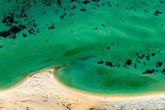 Aerial view of turquoise water meeting a sandy shoreline and reef patches.