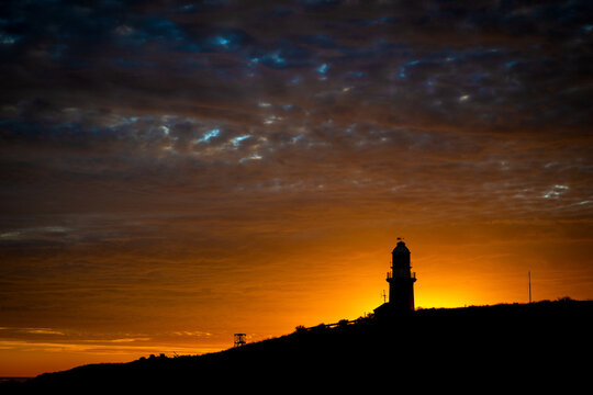 Lighthouse silhouetted against a fiery sunset sky.
