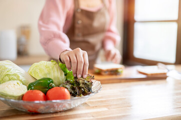 Close up of apron woman holding lettuce making vegetable bread sandwich at kitchen's cooking counter