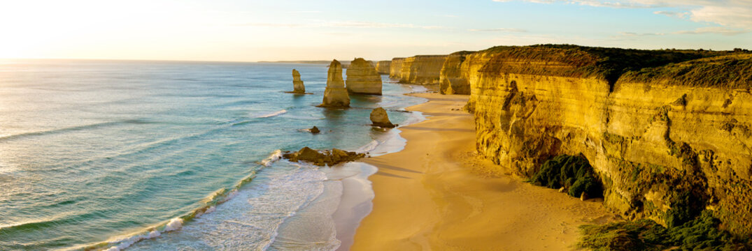 Golden cliffs and sea stacks glow in evening light along a rugged ocean coast.