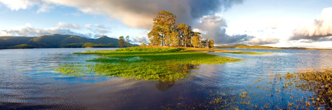 Golden afternoon light over a flooded lakeshore and grassy island surrounded by hills.