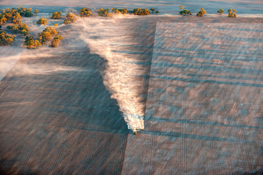 A tractor spreads dust across a wide farmland during cultivation at sunrise.