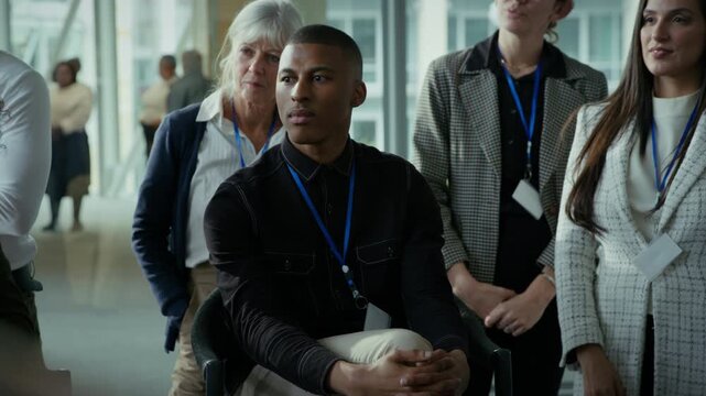 A group of attendees wearing lanyards are attentively listening at a conference or seminar event. They are engaged in the presentation, focused on learning and networking in a corporate setting.