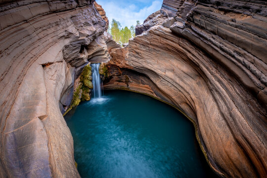 Hidden gorge waterfall plunging into a deep blue rock pool.