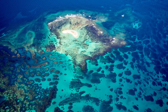 Tiny coral island surrounded by vivid turquoise reef and deep ocean blue.
