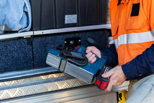 Handyman in workwear holding planer tool by ute