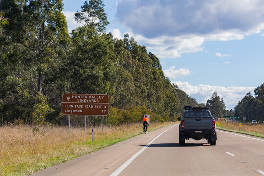 Cyclist on roadside with signage to Hunter valley Vineyards hermitage road and Singleton