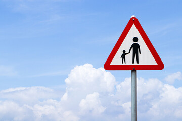School roadside warning sign students or people crossing with blue sky cloud white is background. Symbol white triangular aluminum, red post about pedestrian crossing road sign traffic.