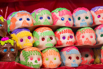 A display of colorful sugar skulls with various shades of green, red, and blue icing. Mexican Day of the Dead tradition, offerings, food, colors, decorations, and papel picado, La Catrina.