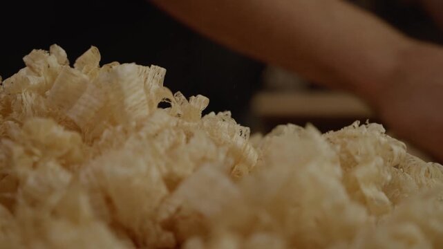 Detailed close-up of fresh wood shavings on a workbench with a blurred background of a craftsman working, symbolizing woodworking, craftsmanship, and handmade furniture creation.