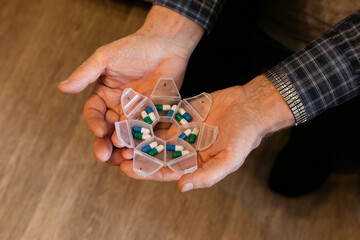 Elderly person organizing medication in weekly pill organizer at home during daytime