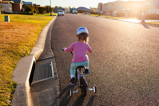 Little girl riding bike down quiet suburban road with backlighting at sunset