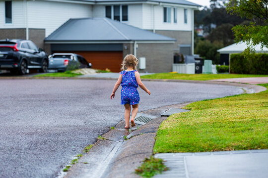 little girl playing in gutter on rainy day running towards drain