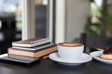 coffee cup with latte coffee and mobile phone, book for read, diary for taking note on black table