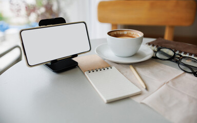 smart phone on stand with coffee cup, note book and diary on table