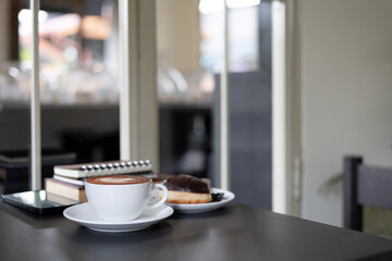 coffee cup with latte coffee and mobile phone, book for read, diary for taking note on black table